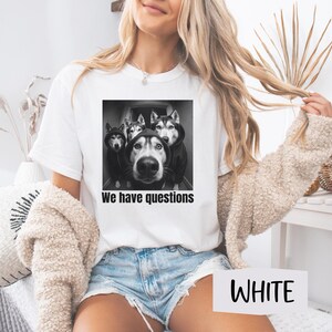 May include: White t-shirt with a black and white image of four Huskies in hoodies, with the text "We have questions". The t-shirt is a crew neck style.
