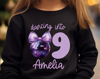 May include: Black sweatshirt with purple text that says "dancing into 9 Amelia" with a purple disco ball and bow.