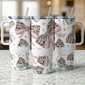 May include: Three stainless steel tumblers with lids and straws. Each tumbler features a white background with a repeating pattern of pink and green bows with leopard print accents.