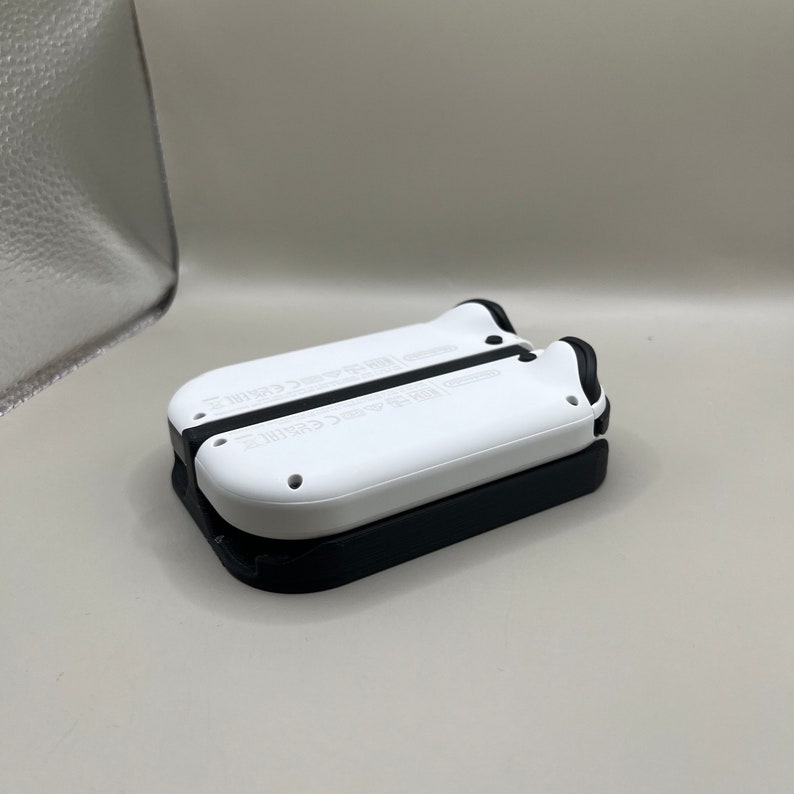 Puede incluir: Dos mandos de juego blancos y negros apilados. Los mandos tienen forma redondeada con detalles negros y peque&ntilde;os agujeros. El mando superior es blanco y el inferior es negro. Probablemente para una consola de juegos.