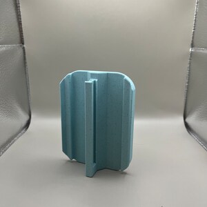 Puede incluir: Objeto de pl&aacute;stico azul claro texturizado, de forma rectangular con asa. El objeto tiene ranuras verticales. El asa es una pieza plana y vertical que se extiende desde la base.