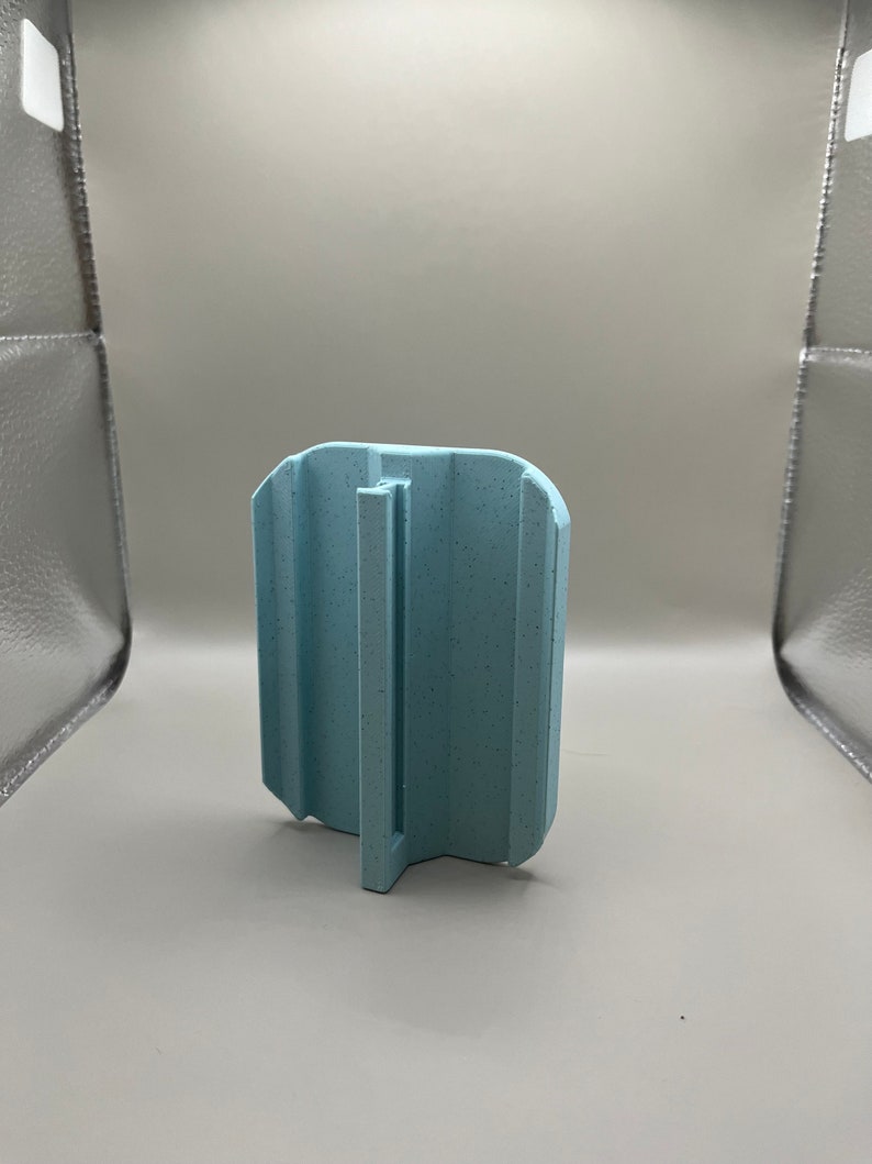 Puede incluir: Objeto de pl&aacute;stico azul claro texturizado, de forma rectangular con asa. El objeto tiene ranuras verticales. El asa es una pieza plana y vertical que se extiende desde la base.