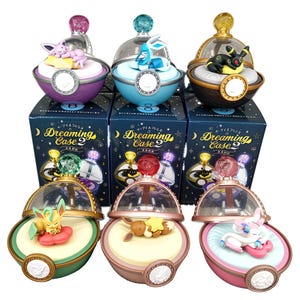 May include: A selection of six decorative figurines, each within a clear, dome-shaped container. The figurines depict various characters, resting on a cream-coloured base. The containers are placed on boxes with the text "Dreaming Case 2".
