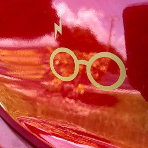 Può includere: Un'auto rossa con un adesivo dorato a forma di fulmine e occhiali sul retro.