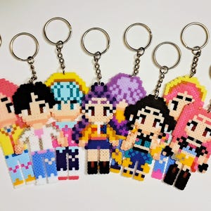 May include: A collection of eight pixel art keychains featuring various characters with different hair colors and outfits. Each keychain has a silver keyring attached. The characters are made of colorful plastic beads.