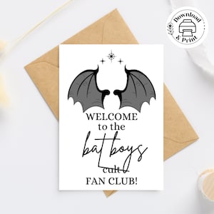 May include: A white card with black text and a black and gray illustration of bat wings. The text reads "Welcome to the bat boys cult FAN CLUB!"