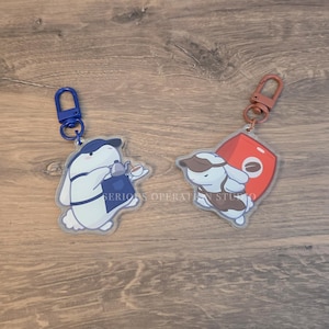 May include: Two acrylic keychains featuring cartoon bunnies. One bunny is holding a teapot and cup, the other is holding a coffee cup. Both keychains have a blue or brown clasp. The text "SERIOUS OPERATION STUDIO" is visible.