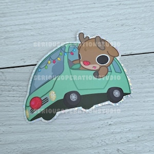 以下が含まれることがあります： 緑色の車を運転する漫画のトナカイが描かれたステッカー。カラフルなクリスマスライトで飾られています。トナカイは茶色の毛皮、大きな黒い目、赤い鼻をしています。車は黒い車輪と赤いフロントライトが付いています。「SERIOUS OPERATIONS STUDIO」の文字が見えます。