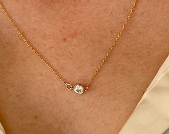 May include: A delicate gold chain necklace with a single, clear round gemstone pendant.