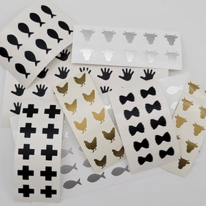 May include: Assortment of black and white sticker sheets with various designs, including fish, handprints, crosses, bows, and cows. The sticker sheets are on a white background.