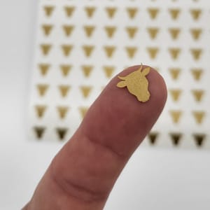 May include: A gold cow sticker on a finger. The sticker is a simple silhouette of a cow's head.