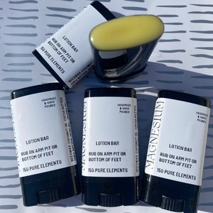 May include: Four black and white lotion bars with the text "LOTION BAR" and "RUB ON ARM PIT OR BOTTOM OF FEET" and "15G PURE ELEMENTS". The bars are made with beeswax, coconut oil, cocoa butter, shea butter, and hemp oil. The bars are labelled "MAGNESIUM" and "HANDMADE & HAND POURED".