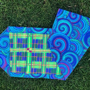 May include: A blue and green fabric table runner with a plaid pattern on one side and a swirling pattern on the other side.