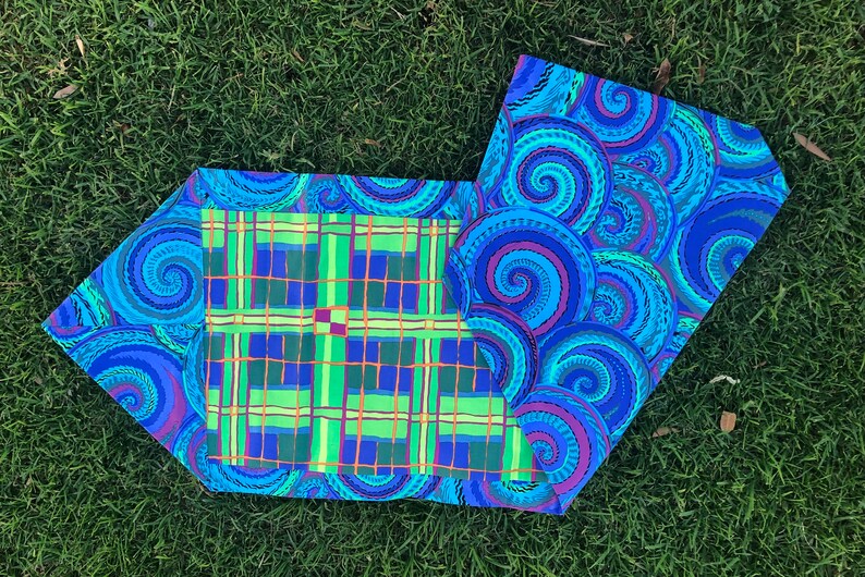 May include: A blue and green fabric table runner with a plaid pattern on one side and a swirling pattern on the other side.