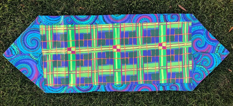 May include: A table runner with a green, blue, and yellow plaid pattern framed by a blue and purple paisley border.