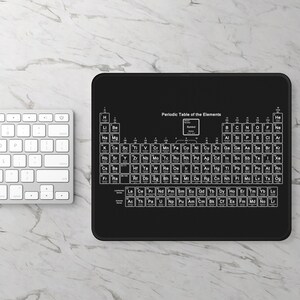 Op de afbeelding: Een zwarte muismat met een witte tabel van het periodiek systeem der elementen erop gedrukt. De tabel bevat het symbool van het element, het atoomnummer en het atoomgewicht.