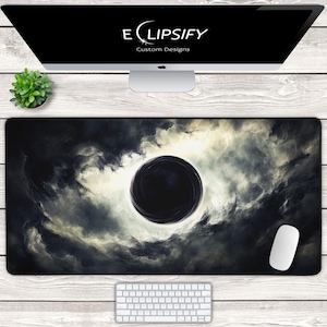 Puede incluir: Alfombrilla de ratón negra y gris con un diseño dramático de nubes arremolinadas y una esfera negra central. El texto "Eclipsify Custom Designs" está en la parte superior. También se ven un ratón y un teclado blancos.