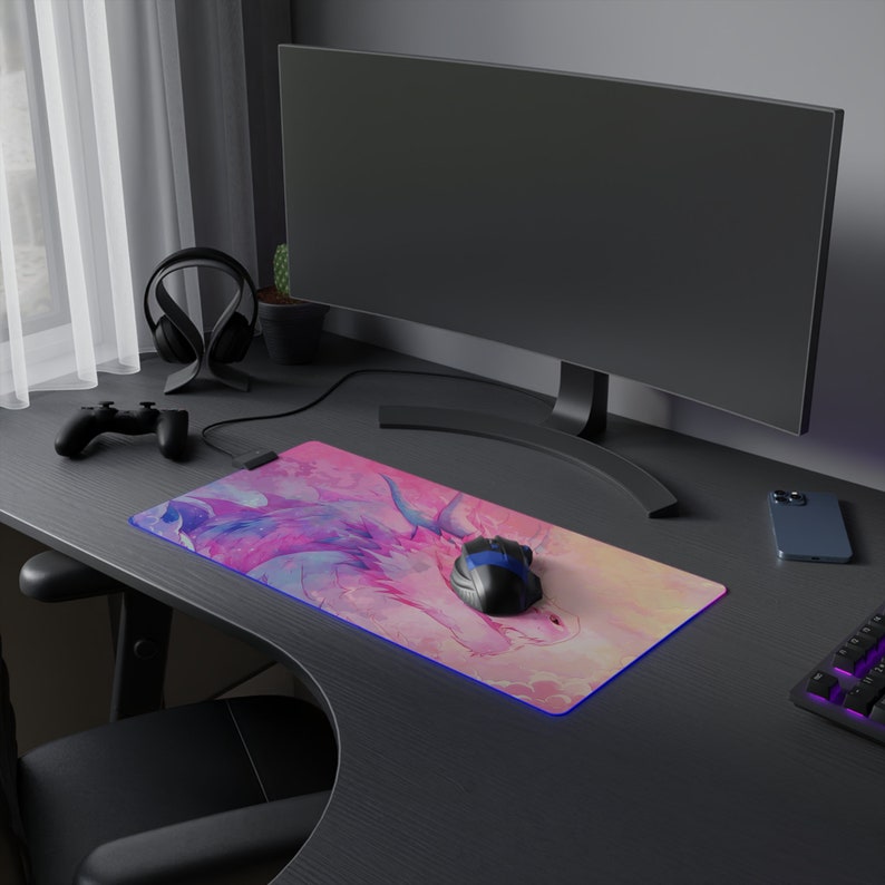 May include: A black desk with a pink and blue dragon-themed mousepad, a black computer mouse, a black wireless controller, a black headset, a potted plant, a black monitor, a black smartphone, and a black keyboard.