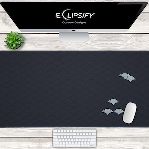 Puede incluir: Una alfombrilla de escritorio azul oscuro con un patrón repetitivo de semicírculos blancos. La alfombrilla tiene tres diseños de olas estilizados blancos en la esquina superior derecha. Un teclado blanco y un ratón blanco están en el escritorio.