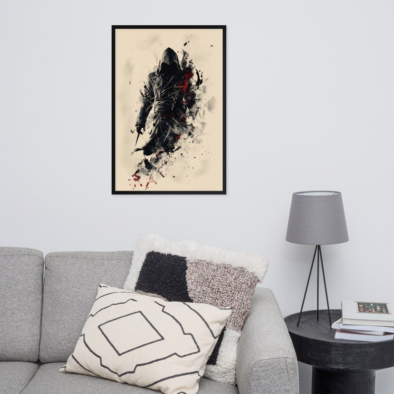 May include: Framed art print featuring a stylized figure in a hooded cloak, holding a blade. The artwork uses a black, red, and beige color palette with a splash effect. The print is displayed in a black frame.