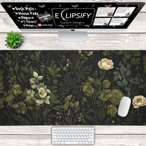 Puede incluir: Una alfombrilla de escritorio negra con un patrón floral con flores blancas y hojas verdes. La alfombrilla está sobre una superficie de madera con un teclado y un ratón de ordenador blanco.