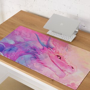 May include: A pink and purple watercolor dragon design on a desk mat. The dragon has a pink snout and blue eyes. The background is a soft pink with white clouds.