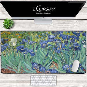 May include: A rectangular mouse mat displaying a painting of blue irises in a garden setting. The artwork has a textured look, with green leaves and yellow flowers. The mat is on a white wooden surface, with a computer mouse and keyboard.
