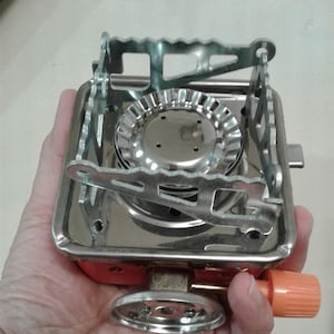 Mini estufa de gas para acampar. Estufa para caminatas, picnics y viajes. Disponible en 2 estilos con y sin manguera trenzada. Soporte para ollas y sartenes y patas extensibles. Portátil