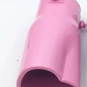 May include: A glossy, pink automotive exhaust tip. The metal component has a curved shape with a rounded opening and a small fitting on top. The exhaust tip is designed to be installed on a vehicle's exhaust system.