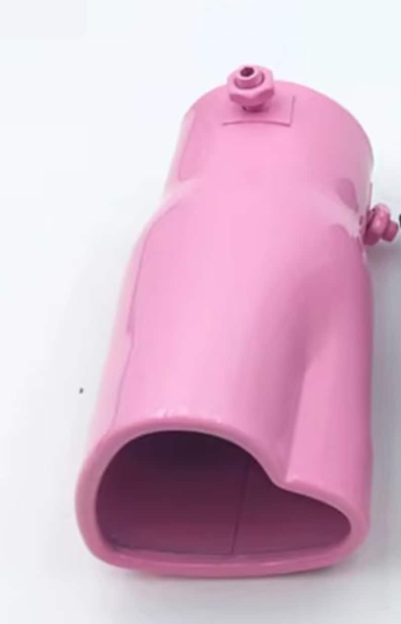 May include: A glossy, pink automotive exhaust tip. The metal component has a curved shape with a rounded opening and a small fitting on top. The exhaust tip is designed to be installed on a vehicle's exhaust system.