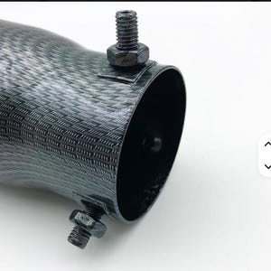 May include: Close-up of a dark gray, textured metal tube with a black interior. Two black bolts secure the tube. The tube has a woven pattern and a curved shape.