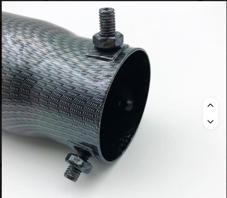 May include: Close-up of a dark gray, textured metal tube with a black interior. Two black bolts secure the tube. The tube has a woven pattern and a curved shape.