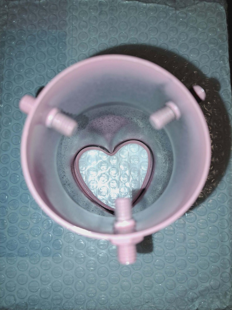 May include: A pink, cylindrical object with three protruding bolt-like structures and a heart-shaped cutout at the base. The object is set against a blue bubble wrap background, creating a contrast in textures and colors.