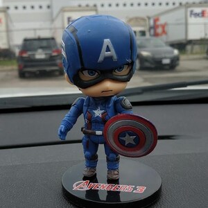 May include: A blue and red Captain America figurine holding a shield with a star. The figurine is standing on a black base with the words "Avengers 3" printed on it.