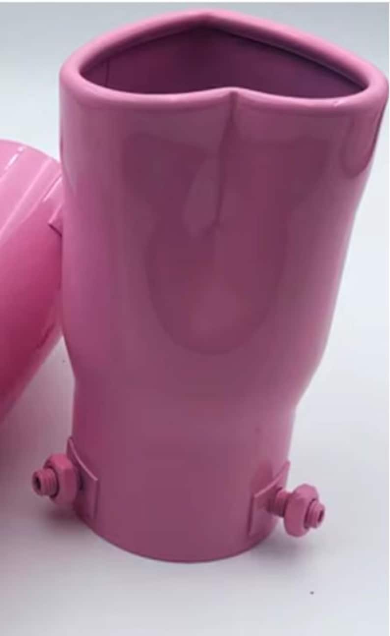 May include: A pair of pink exhaust tips with a heart-shaped opening. The tips are made of metal and have a glossy finish. Each tip has a bracket with a bolt and nut for mounting.
