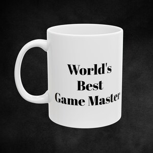 Puede incluir: Taza de café de cerámica blanca con texto negro que dice "World's Best Game Master".
