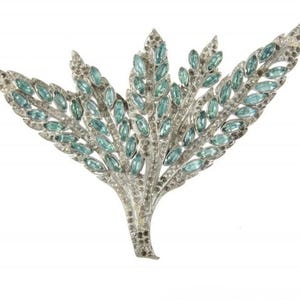 May include: A silver tone brooch with a design of multiple leaves set with light blue rhinestones.