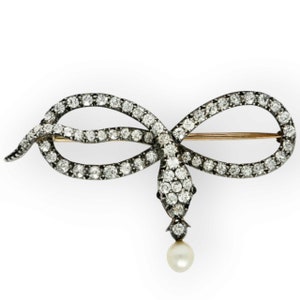May include: A silver and gold snake brooch with a pearl pendant. The snake is set with diamonds and is in a knotted position.