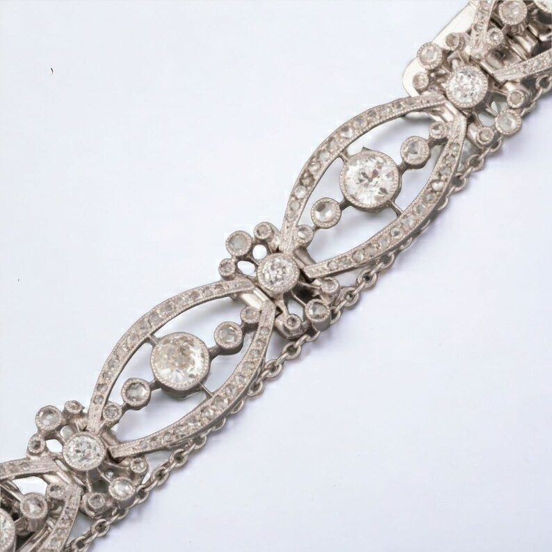 May include: A silver bracelet with an intricate design. The bracelet features multiple oval-shaped links, each adorned with small, sparkling stones and larger, round gemstones. Delicate chain links connect the decorative sections.