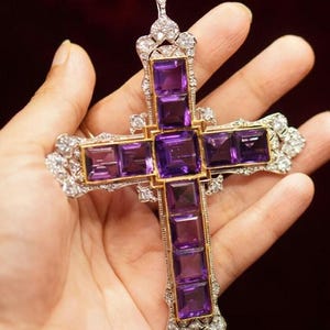 May include: A large, ornate cross pendant with a gold frame and purple amethyst stones. The cross is set with smaller diamonds around the edges.