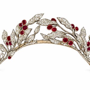 Könnte beinhalten: Ein Diadem mit einem metallischen Band in Form von Zweigen mit Blättern und Beeren. Die Blätter sind mit zahlreichen kleinen klaren Steinen besetzt, während die runden Beeren mit tiefroten Steinen verziert sind, was ein botanisches Design ergibt.