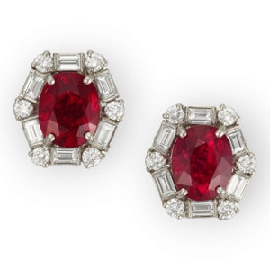 Può includere: Un paio di orecchini con rubino e diamanti. Ogni orecchino presenta un grande rubino di forma ovale circondato da un'aureola di diamanti più piccoli. I diamanti sono incastonati in una montatura in platino.