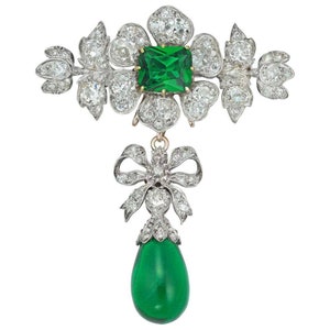 Pode incluir: Um broche vintage de esmeralda e diamantes com um pingente de esmeralda em forma de lágrima. O broche apresenta uma esmeralda central cercada por diamantes e um design em forma de laço com diamantes.