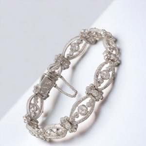 May include: An ornate silver bracelet with a delicate, openwork design. The bracelet features a series of oval links, each adorned with sparkling gemstones. The clasp is visible, and the overall aesthetic is elegant and timeless.