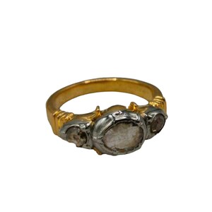 Op de afbeelding: Een gouden ring met drie heldere, gefacetteerde stenen gezet in zilver. De middelste steen is groter dan de twee stenen aan weerszijden.