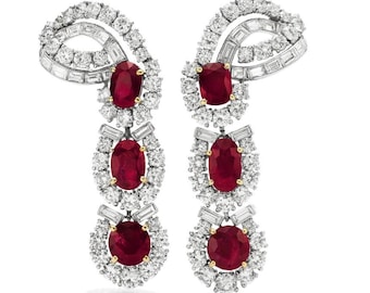 Puede incluir: Un par de pendientes colgantes con un engaste plateado y tres piedras de rubí rojo en cada pendiente. Las piedras de rubí están rodeadas de diamantes más pequeños.