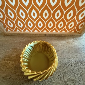 May include: A gold-coloured, decorative bowl with a swirling, textured design. The bowl is empty and appears to be made of ceramic.