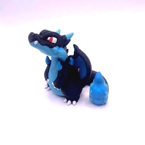 Könnte beinhalten: Handgefertigte Drachenfigur in Schwarz und Blau, mit roten Augen und weißen Krallen. Der Drache sitzt, mit einer kleinen, losen blauen Flamme. Diese Fantasiefigur ist ein einzigartiges Sammlerstück.