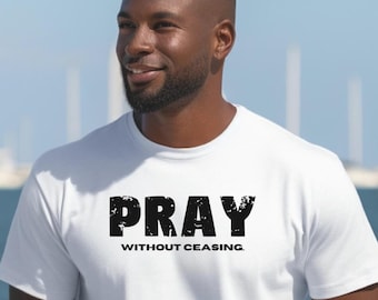 May include: A white t-shirt with the words "PRAY" above "WITHOUT CEASING" in black, distressed font. The shirt is being worn by a person standing near the water with sailboats in the background.
