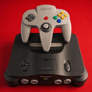 Consola oficial Nintendo 64 negra, mando OEM N64, adaptador de corriente y cable AV incluidos.